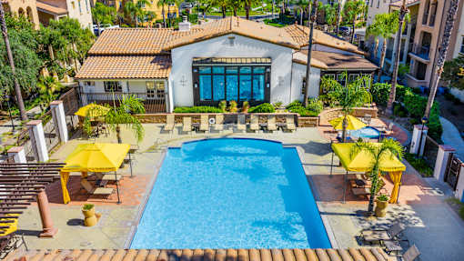 A pool surrounded by yellow sun shades and a white building with a blue door.