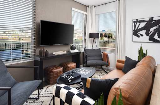 A living room with a brown leather couch, a black and white checkered rug, and a flat screen TV mounted on the wall.