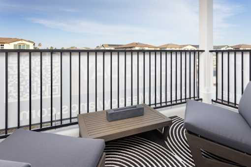 A balcony with a black railing, a wooden coffee table, and two grey cushions.