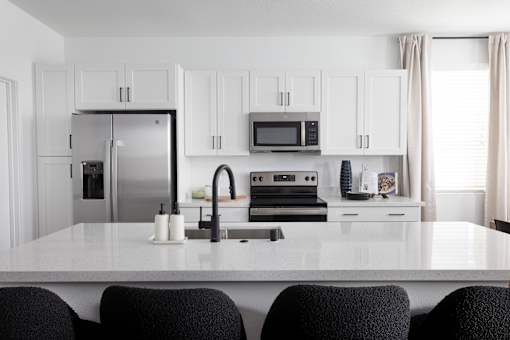 a kitchen with white cabinets and a large white island with black chairs