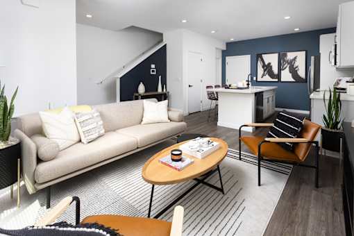 a living room with a couch table and chairs and a kitchen in the background