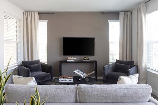 A living room with a grey couch, a black television, and two chairs.