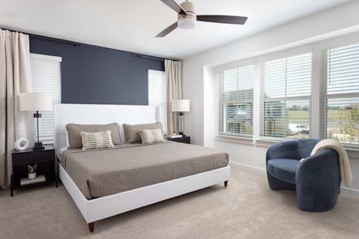 A bedroom with a large bed, a ceiling fan, and a chair.