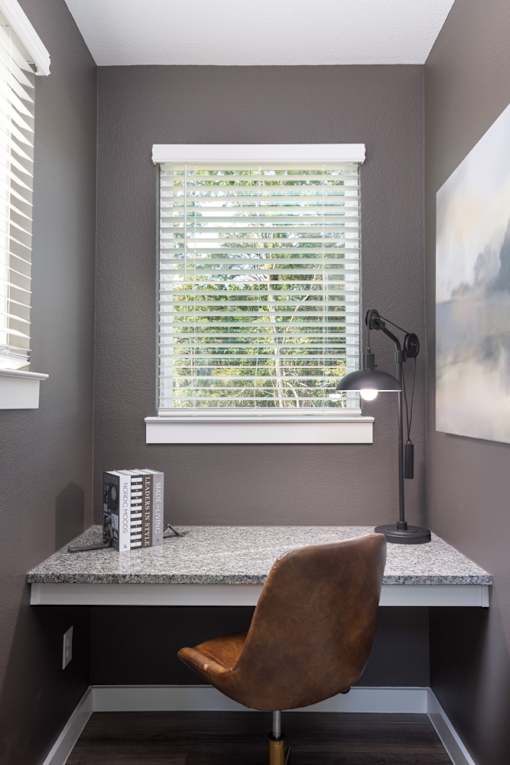 A brown chair is in front of a desk with a lamp on it.