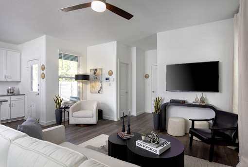 A living room with a white couch, a black coffee table, and a flat screen TV mounted on the wall.