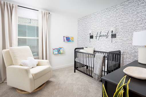 A baby's room with a white rocking chair and a black crib.