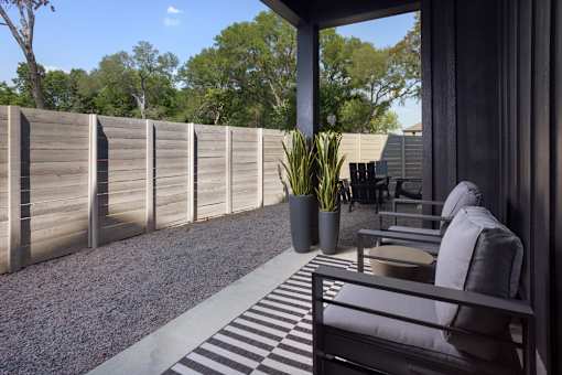 A patio with a bench, potted plant, and a fence.