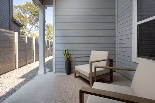 A chair sits on a porch with a potted plant next to it.