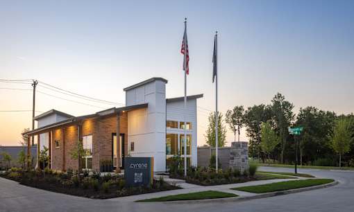 The image shows a building with the name "Sylene" on it, surrounded by a well-maintained lawn and a clear sky above.