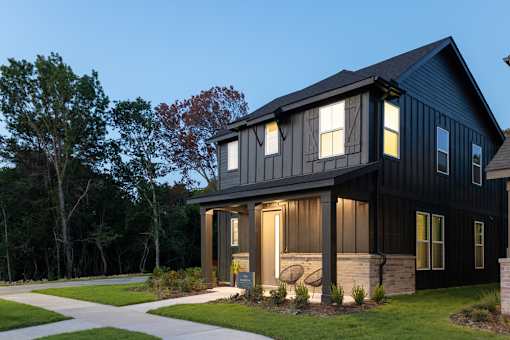A modern black house with a well-maintained lawn and trees in the background.