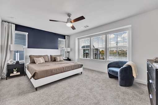 A bedroom with a bed, chair, and a ceiling fan.