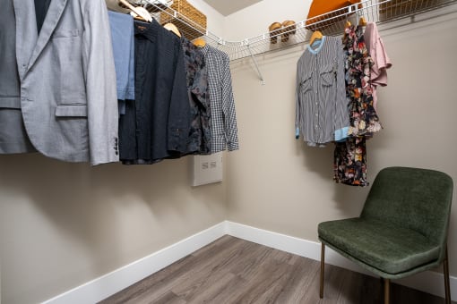 a walk in closet with a chair and clothes hanging on the wall