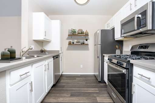 A kitchen with white cabinets and black appliances. at 55+ FountainGlen Terra Vista, California, 91730