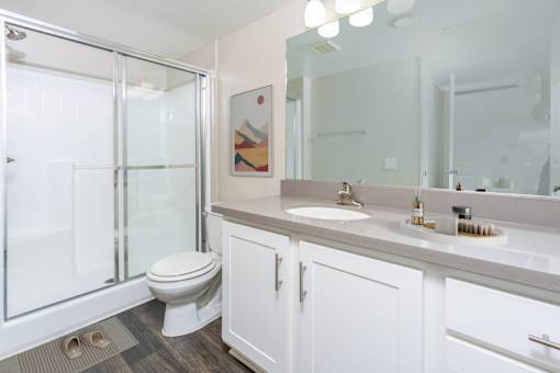 A bathroom with a toilet, sink, mirror and shower. at 55+ FountainGlen Terra Vista, Rancho Cucamonga, 91730