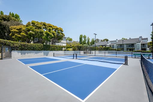 A tennis court with blue and white markings surrounded by greenery and buildings.