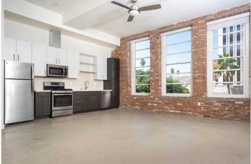 apartment unit kitchen with stainless steel appliances and a brick wall with large windows. at Imperial Hardware Lofts, California