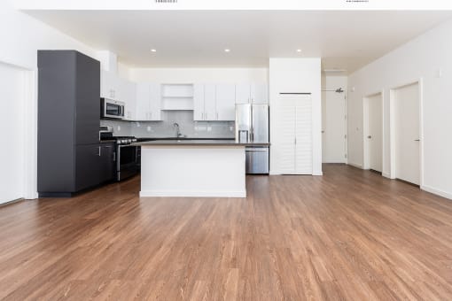 an empty living room with a kitchen and white cabinets at Imperial Hardware Lofts, Riverside, CA