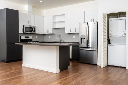 kitchen with stainless appliances, white cabinets, stackable washer and dryer at Imperial Hardware Lofts, California
