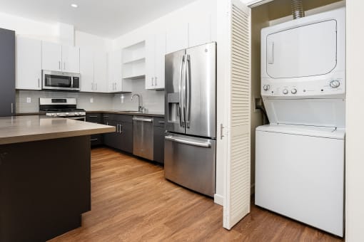 White stackable washer and dryer, kitchen with stainless appliances at Imperial Hardware Lofts, Riverside