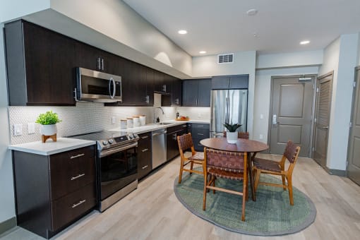Apartments Burlingame, CA - Eat-In Kitchen With Dining Room Table, Black Cabinets, White Countertops, And Stainless-Steel Appliances.