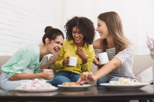 a group of women sitting on a couch eating food and drinking coffee