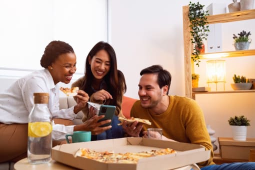 a group of people sitting around a table eating pizza and looking at a cell phone