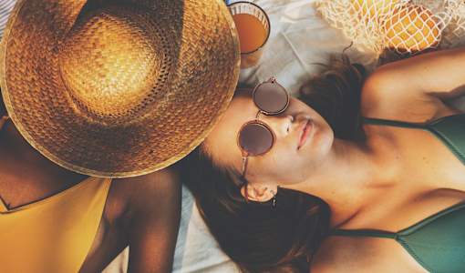 A woman in a green bikini and straw hat is lying on a white surface.