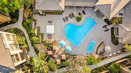 An aerial view of a swimming pool surrounded by a garden and buildings.