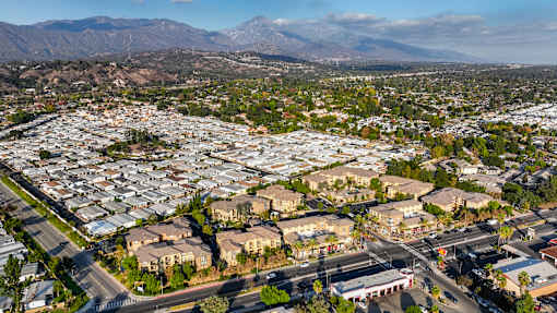A residential area with houses and streets in the foreground and mountains in the background.