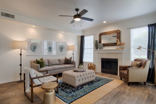 Apartments Plano, TX - McDermott Place - Living Room With Tan Couch, Area Rug, Fireplace, Two Windows, And A Ceiling Fan.