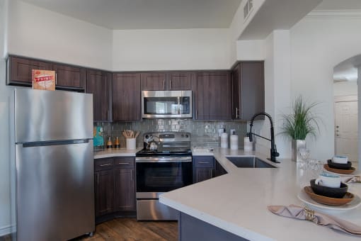 Plano, TX Apartments- McDermott Place - Kitchen With Dark Wood Cabinets, White Countertops, Grey Backsplash, And Appliances.