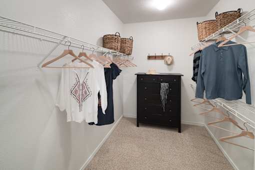 a walk in closet with clothes hanging on racks and a dresser at McDermott Place, Plano, Texas