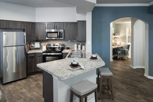 Chef-Inspired Kitchen with Wood-Style Flooring, Stainless Steel Appliances, Breakfast Bar with Barstools, and Wood-Tone Cabinets at McDermott Place, Plano
