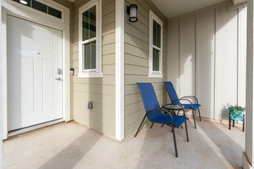 a porch with two blue chairs and a white door
