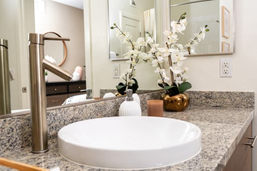 a bathroom sink with a mirror and a vase of flowers at Miro at the Parc, Henderson, 89074