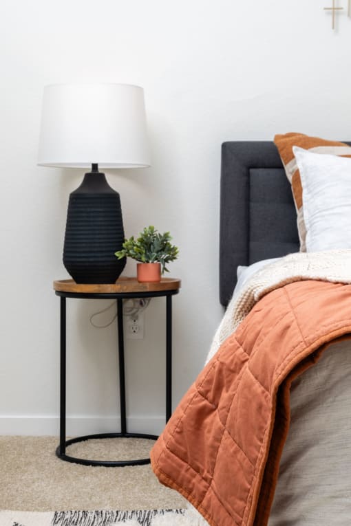 a bedroom with a bed and a table with a lamp and a plant