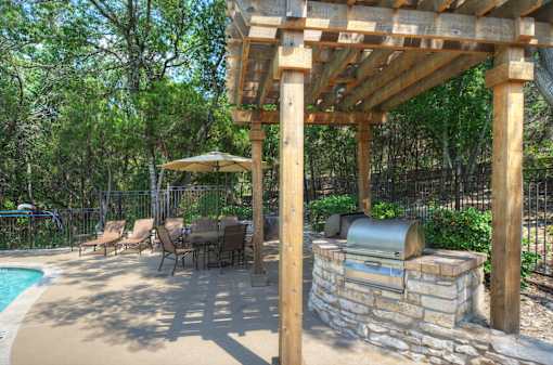 A wooden pergola over a table with chairs and a grill next to a pool.