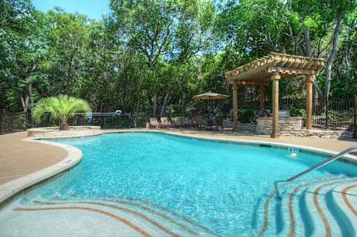 A pool with a wooden pergola in the background.