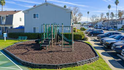 A playground with a green slide and brown mulch in the foreground. at Nola 624, West Covina
