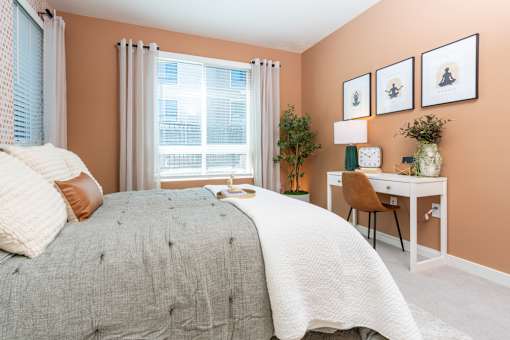 2 Bedroom Luxury Apartments in Riverside, CA - North Grove - Cozy Bedroom With Large Window And Curtains, Soft Bedding, Accent Pillows, And Workspace Desk Beside Seating Chair