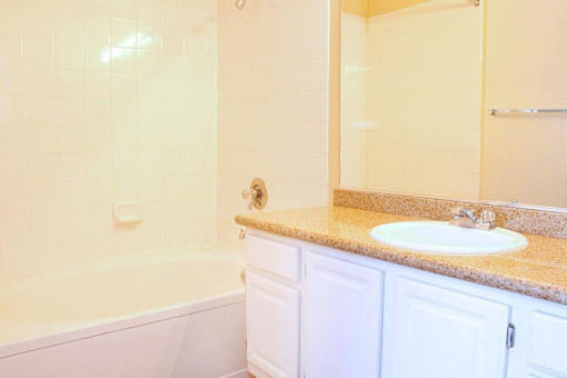 A white bathroom with a tub, sink, and mirror at Avalon at Seven Hills Apartments, Henderson
