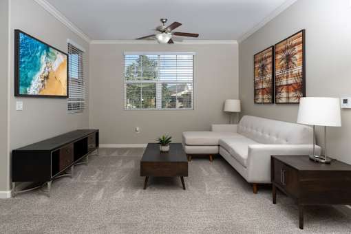 A living room with a white couch, a television, and a ceiling fan.