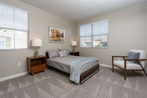 A bedroom with a bed, chair, and two lamps.