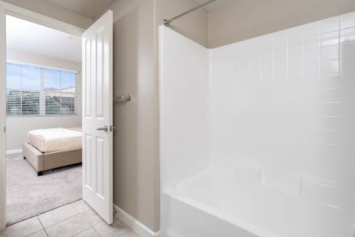 A white bathroom with a tub and a bed in the corner.