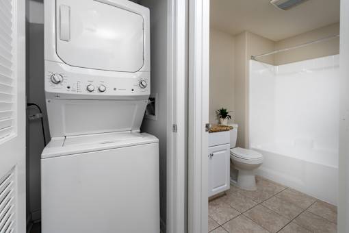 A white washing machine is in a small bathroom with a toilet and a sink.