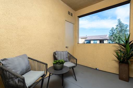 A balcony with a chair, table and potted plant.