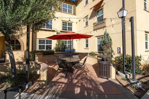A patio with a table and chairs under a red umbrella.