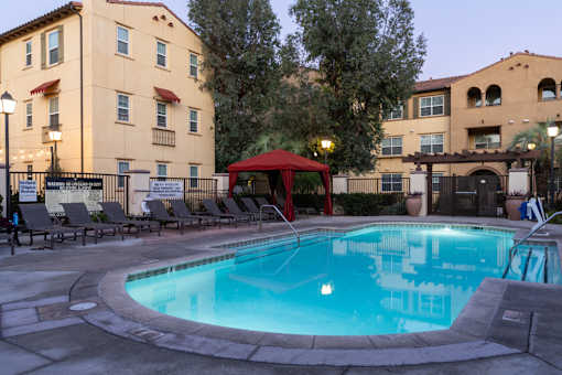 A swimming pool surrounded by lounge chairs and umbrellas in front of a building.