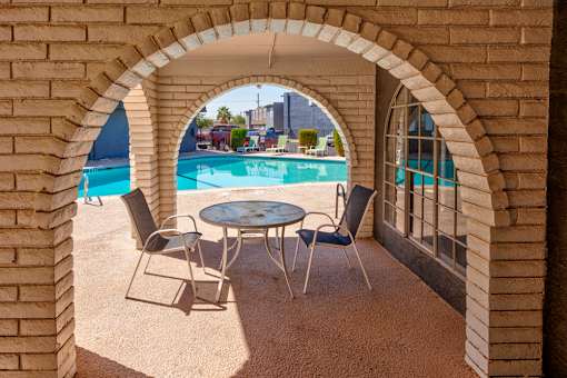 A table and chairs are set up on a patio with a pool in the background.