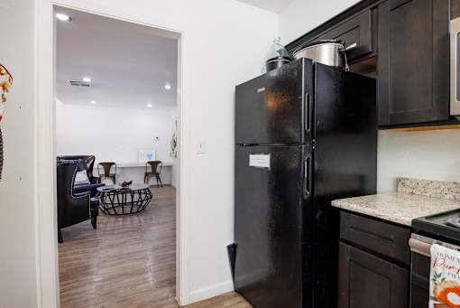 A black refrigerator is in a kitchen with a dining table and chairs in the background.